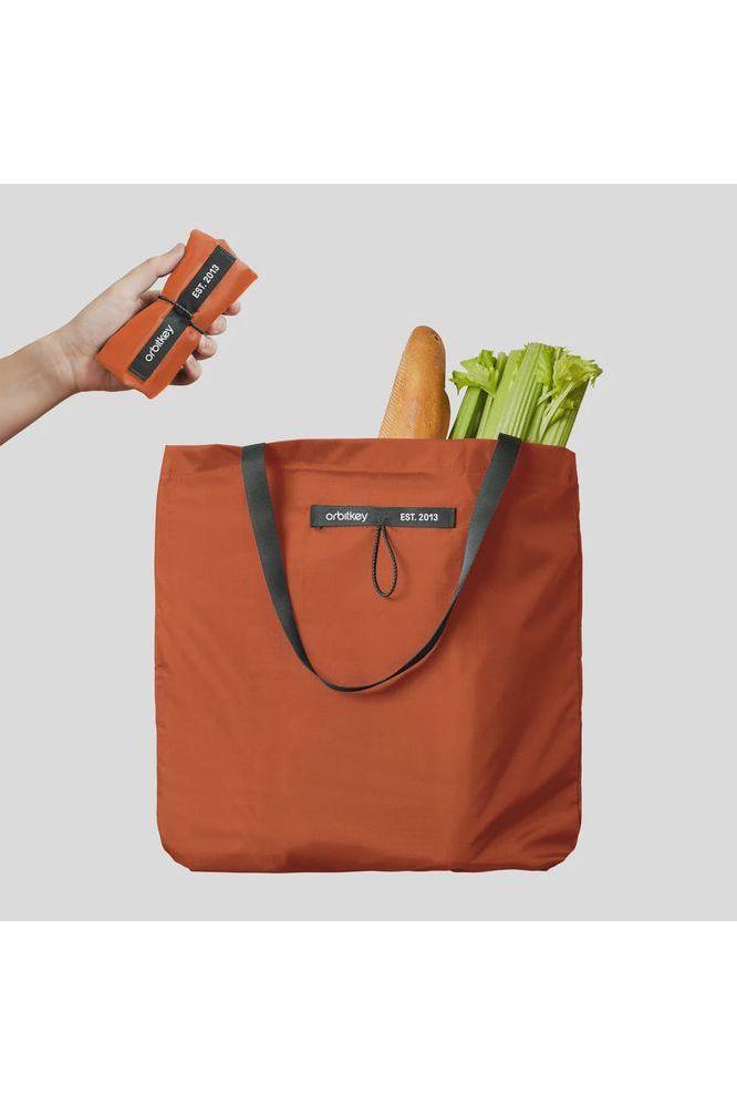 Orbitkey-Foldable-Tote-Bag-Limited-Edition-Tangerine-Colour--Image-shows-bag-with-groceries-in-and-the-bag-folded-and-being-held-by-a-hand---Crisp-Home---Wear