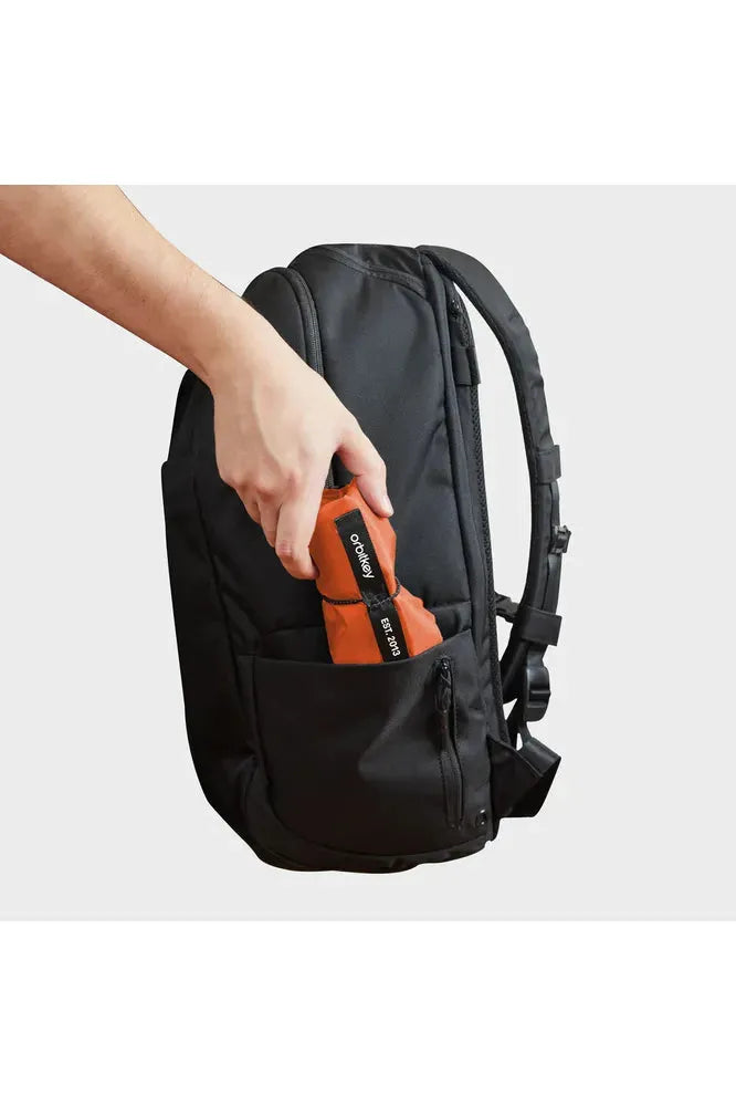 Orbitkey_Foldable_Tote_Limited_Edition_Tangerine._Image_shows_tote_rolled_being_placed_in_the_side_pocket_of_a_backpack._Crisp_Home_Wear.