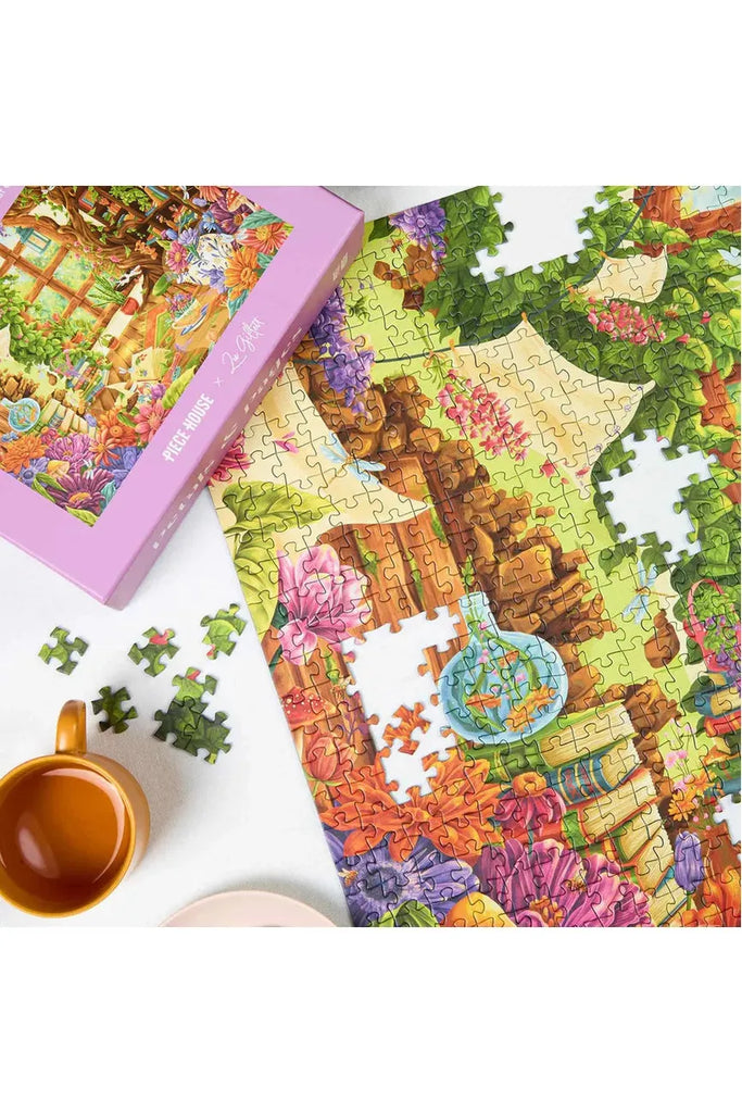 Piece House and Zoe Gillett collaboration jigsaw puzzle titled 'Petals & Pages.' The image shows the puzzle's partially completed design, sitting beside its box and a cup on a white surface.