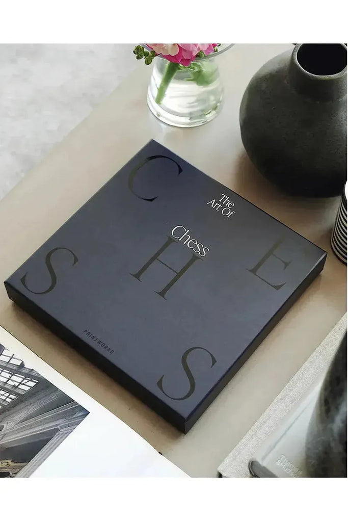 Printworks presents an Art of Chess game in a book-like box titled 'The Art of Chess,' placed on a table with decorative items. 