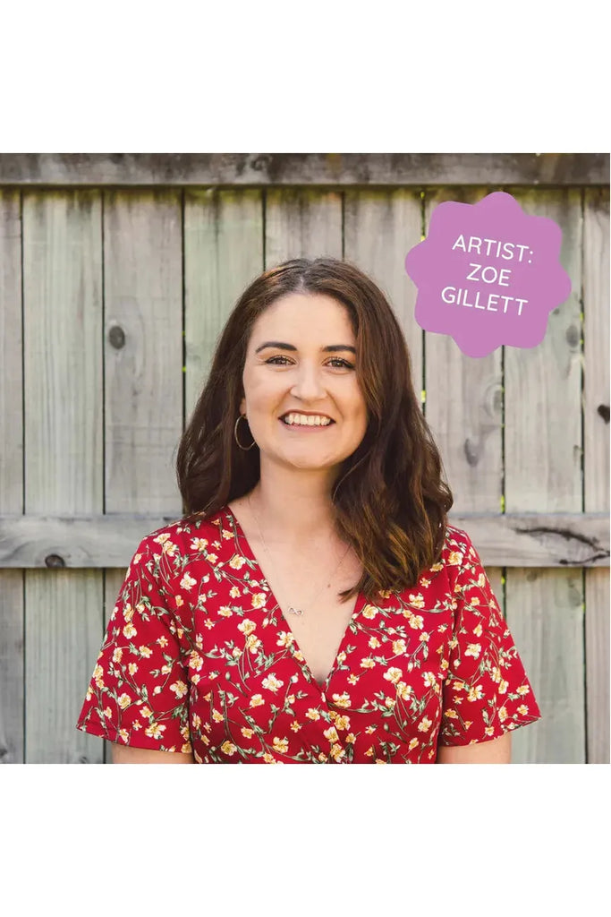 Piece House and Zoe Gillett have collaborated on a jigsaw puzzle titled 'Petals & Pages.' The image features artist Zoe Gillett in a red floral dress standing in front of a wooden fence.