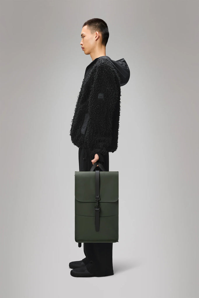 Khaki Green backpack with a black strap on a light gray background. Rains Green backpack.