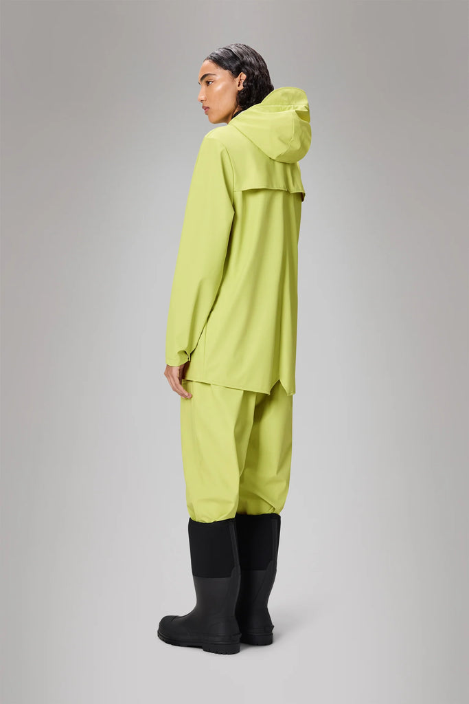 Person wearing a bright green Rains raincoat in acid colourway on a grey background