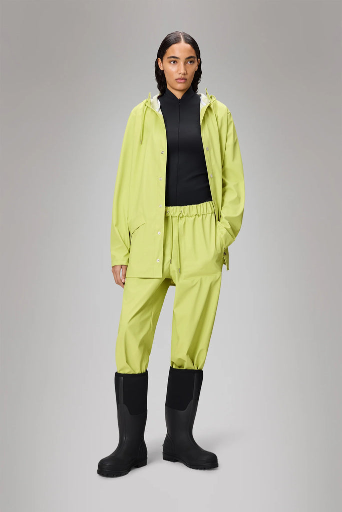Person wearing a bright green Rains raincoat in acid colourway on a grey background