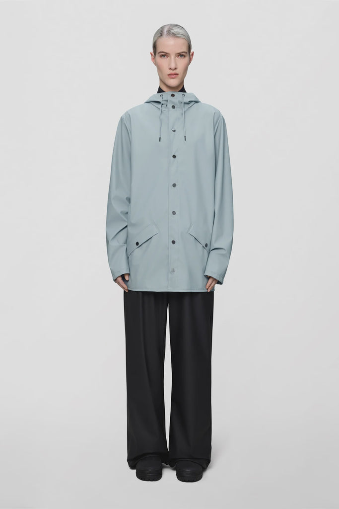 Person wearing a light blue raincoat on a plain background. Rains Jacket in Pool.