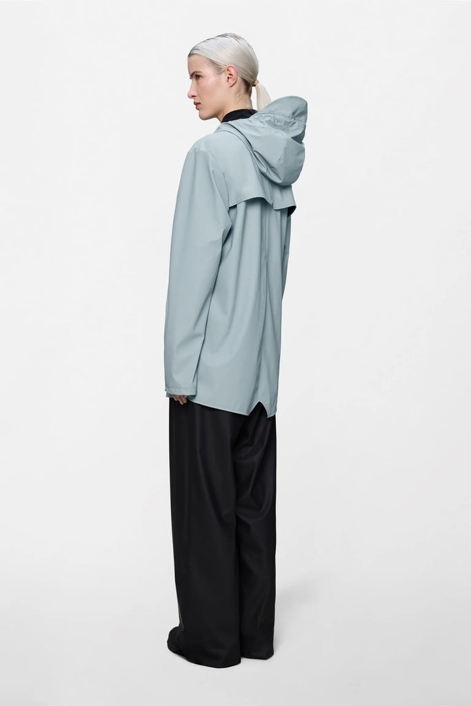 Person wearing a light blue raincoat on a plain background. Rains Jacket in Pool.