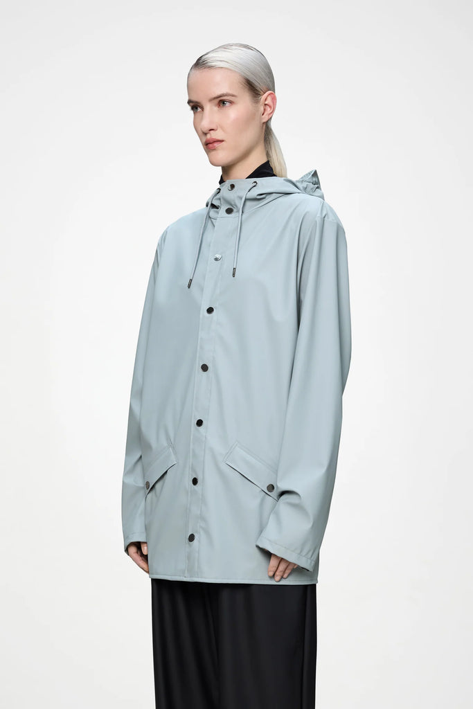 Person wearing a light blue raincoat on a plain background. Rains Jacket in Pool.