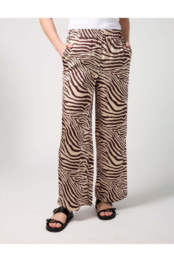 Woman wearing a zebra print pant and white tee on a white background. Stella and Gemma Jenna Pant in Merlot Zebra.