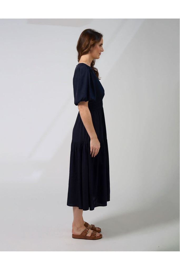 Woman wearing a navy blue Sabrina dress from New Zealad Label Stella and Gemma on a white background side view