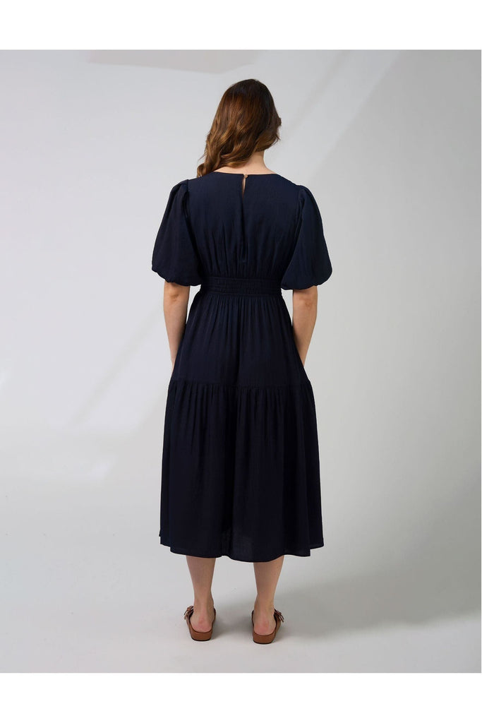 Woman wearing a navy blue Sabrina dress from New Zealad Label Stella and Gemma on a white background back view