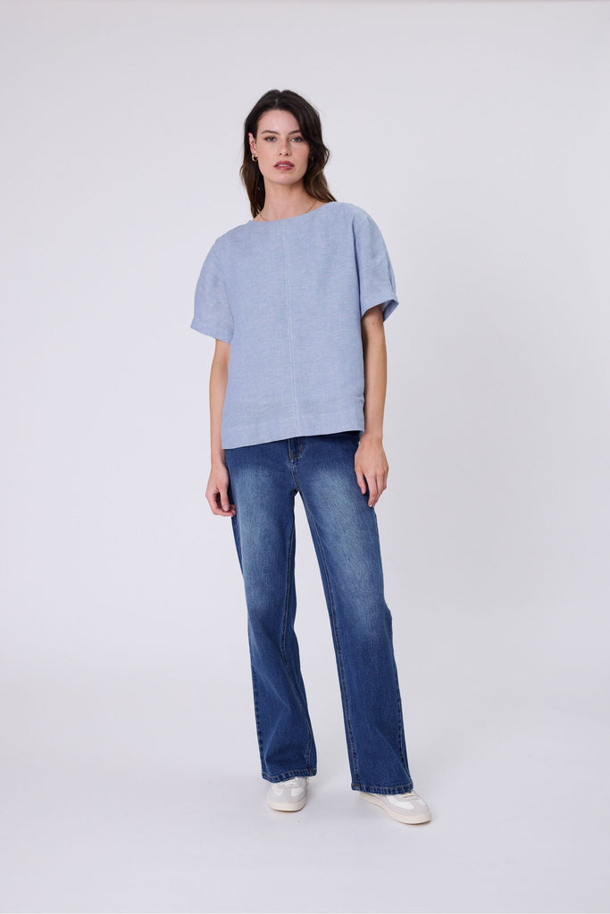Woman wearing a light blue top and blue jeans on a white background. Marlow Sable Linen Top Blue Smoke.