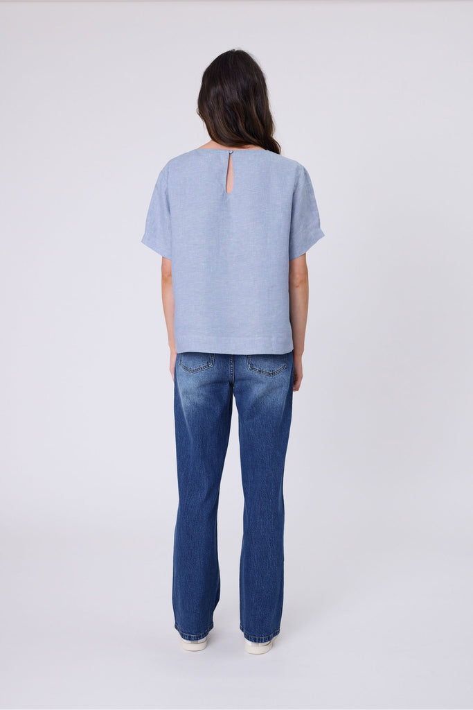Woman wearing a light blue top and blue jeans on a white background. Marlow Sable Linen Top Blue Smoke.