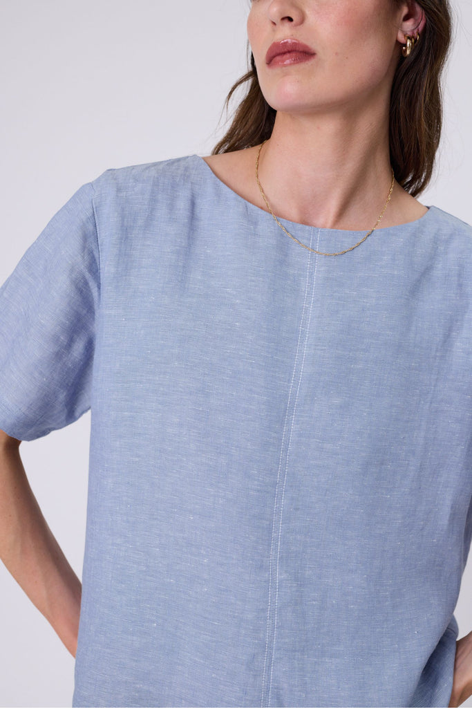 Woman wearing a light blue top and blue jeans on a white background. Marlow Sable Linen Top Blue Smoke.