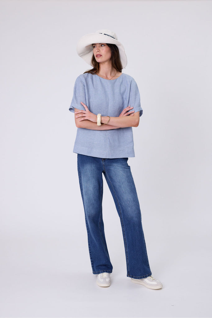 Woman wearing a light blue top and blue jeans on a white background. Marlow Sable Linen Top Blue Smoke.