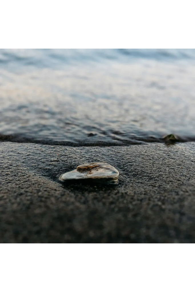 Heart-shaped stone on wet sand with water in the background.