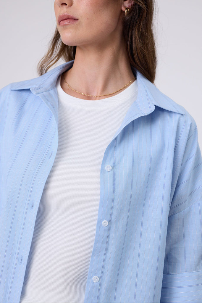 Woman wearing a light blue striped shirt andwhite tee on a white background. Marlow Shoreline Shirt.