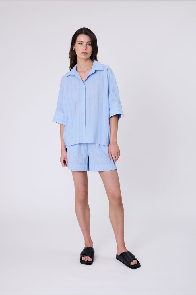 Woman wearing light blue striped shorts and matching shirt on a white background