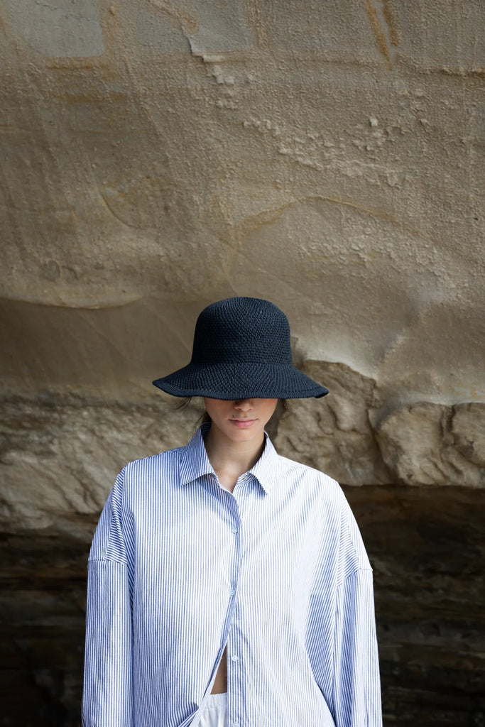 Woman wearing a black hat in a desert-like setting. Sophie Travelling Hat in Black.