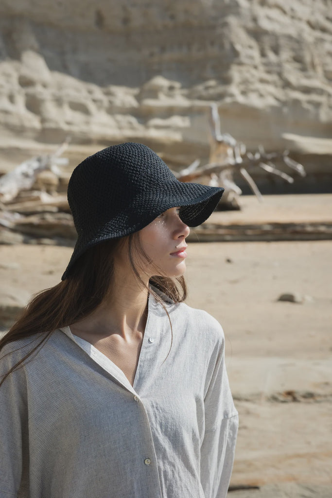 Woman wearing a black hat in a desert-like setting. Sophie Travelling Hat in Black.