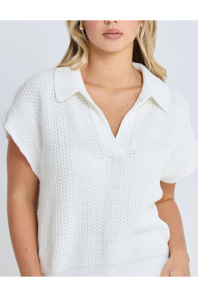 Woman wearing a white sleeveless sweater against a plain background.