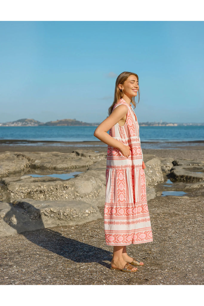 Woman in a patterned dress standing on a rocky beach with ocean and sky in the background