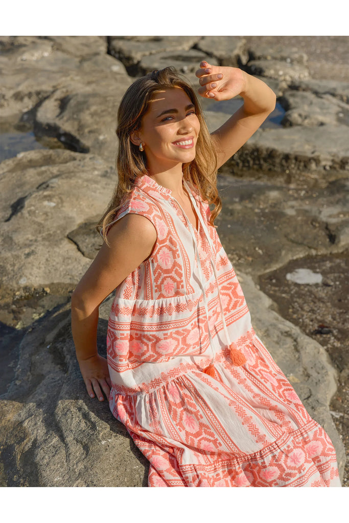 Woman in a pink dress sitting on rocks by the water