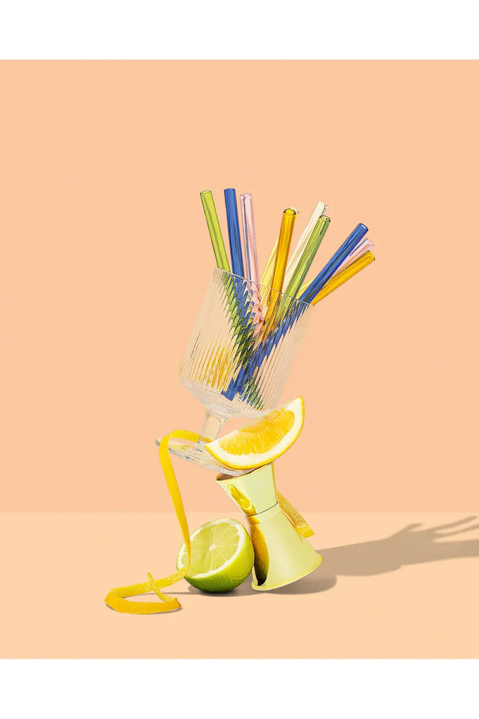 Sucker Colourful cocktail straws in a cocktail glass with lemon and lime on a peach background.