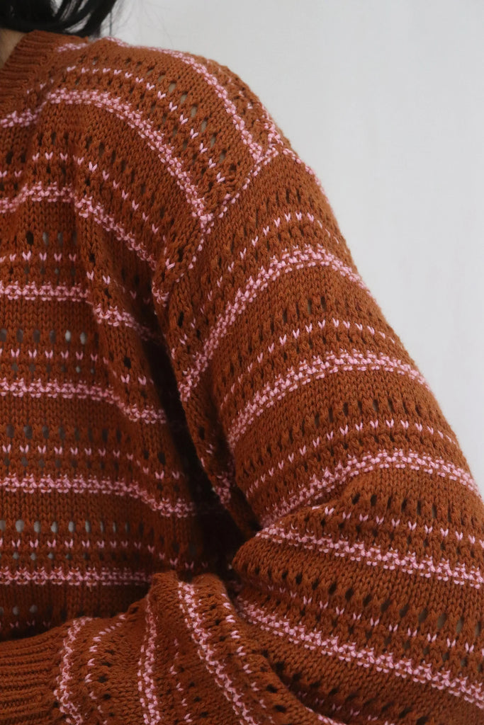 Woman wearing a brown and pink striped sweater against a white background. Tatano Cotton Trellis V Neck Sweater in rust and peony.