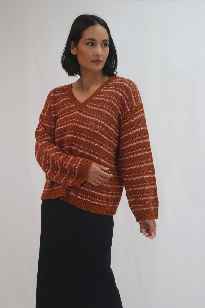 Woman wearing a brown and pink striped sweater against a white background. Tatano Cotton Trellis V Neck Sweater in rust and peony.