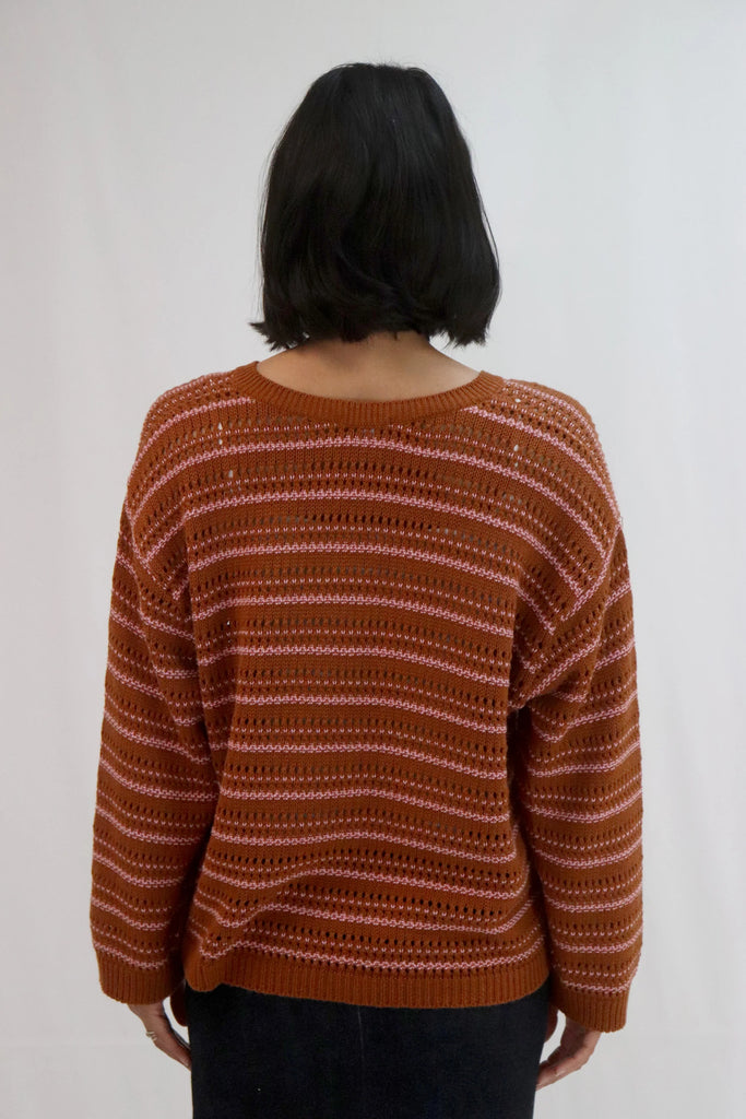Woman wearing a brown and pink striped sweater against a white background. Tatano Cotton Trellis V Neck Sweater in rust and peony.