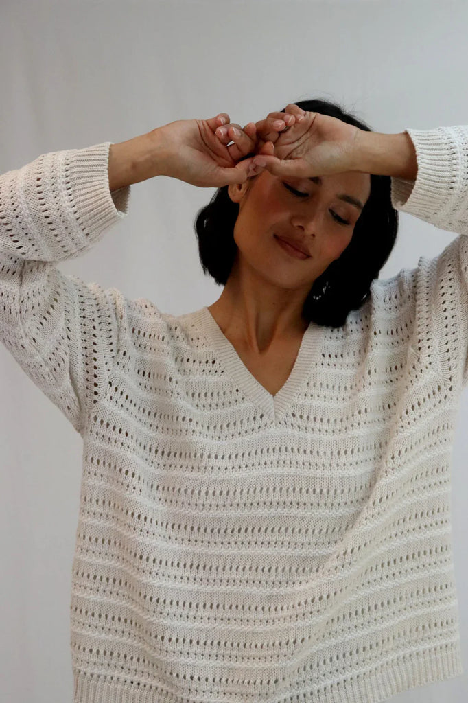 Woman wearing a beige crochet sweater against a white background. Tatano Trellis V Neck Sweater in Sand and White.
