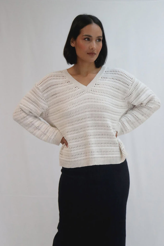 Woman wearing a beige crochet sweater against a white background. Tatano Trellis V Neck Sweater in Sand and White.