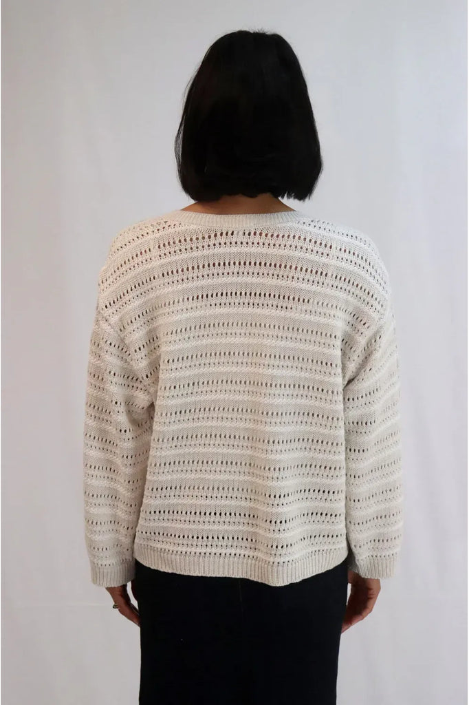 Woman wearing a beige crochet sweater against a white background. Tatano Trellis V Neck Sweater in Sand and White.