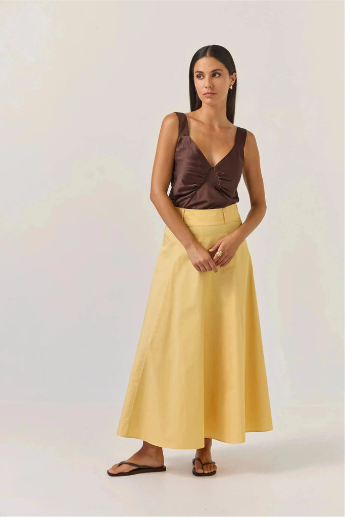Woman wearing a brown satin top and Tuesday Label Circle Skirt in gold on a white background