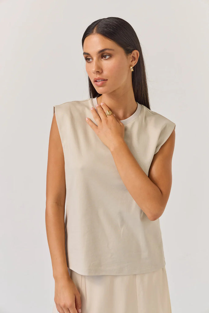 Woman wearing a beige sleeveless tank top on a plain background. Tuesday Noon Tank in Cement.