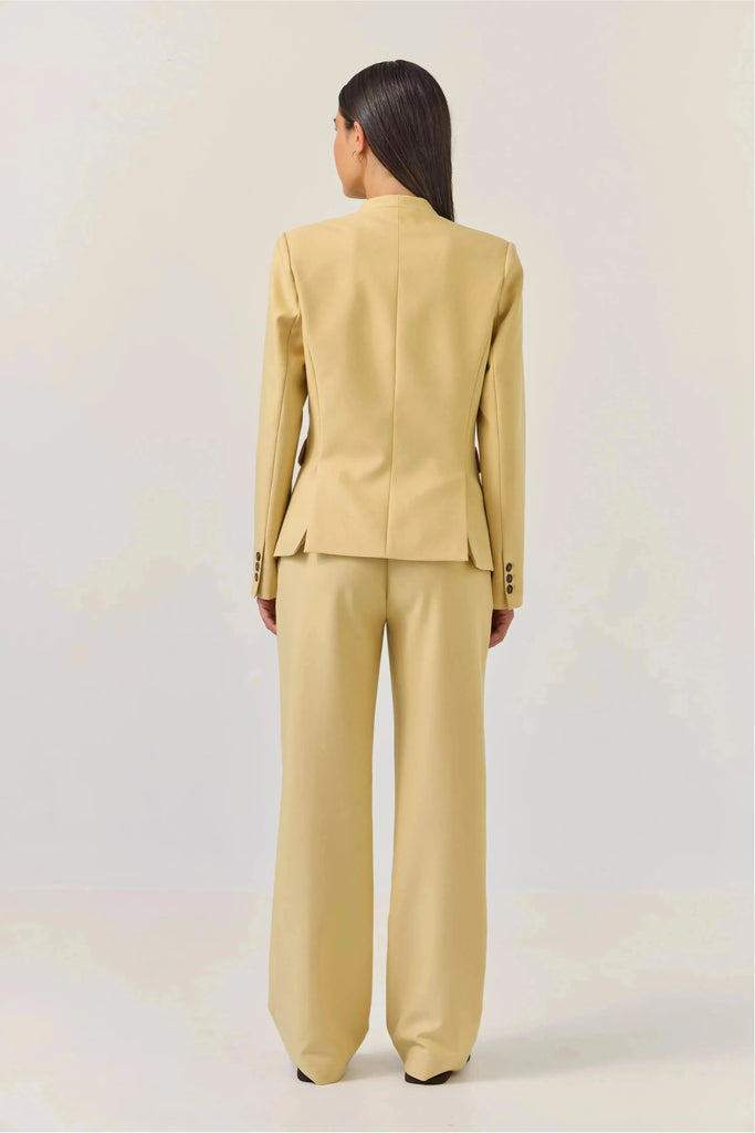 Woman wearing a Tuesday Label Tuxedo Blazer, butter lemon with a matching pant on a plain background back view