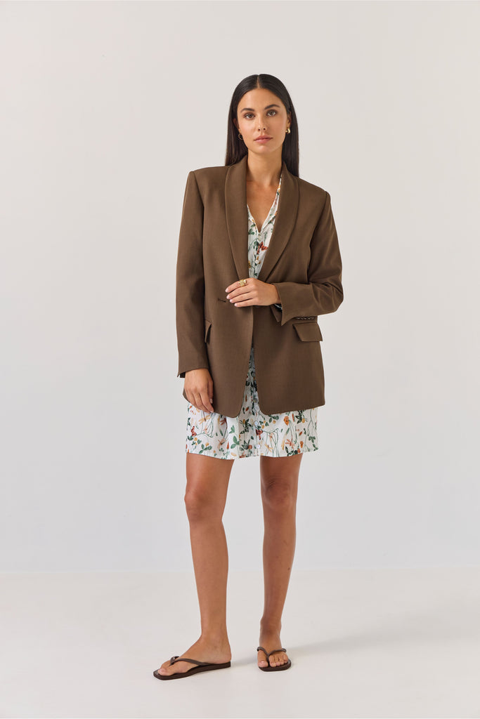 Woman wearing a brown blazer over a floral dress on a white background
