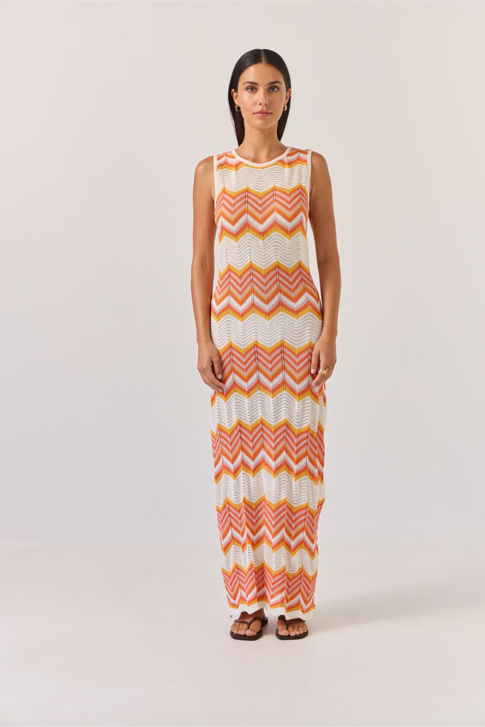 Woman wearing a sleeveless dress with orange and white zigzag pattern on a plain background. Tuesday Label Horizon Dress.