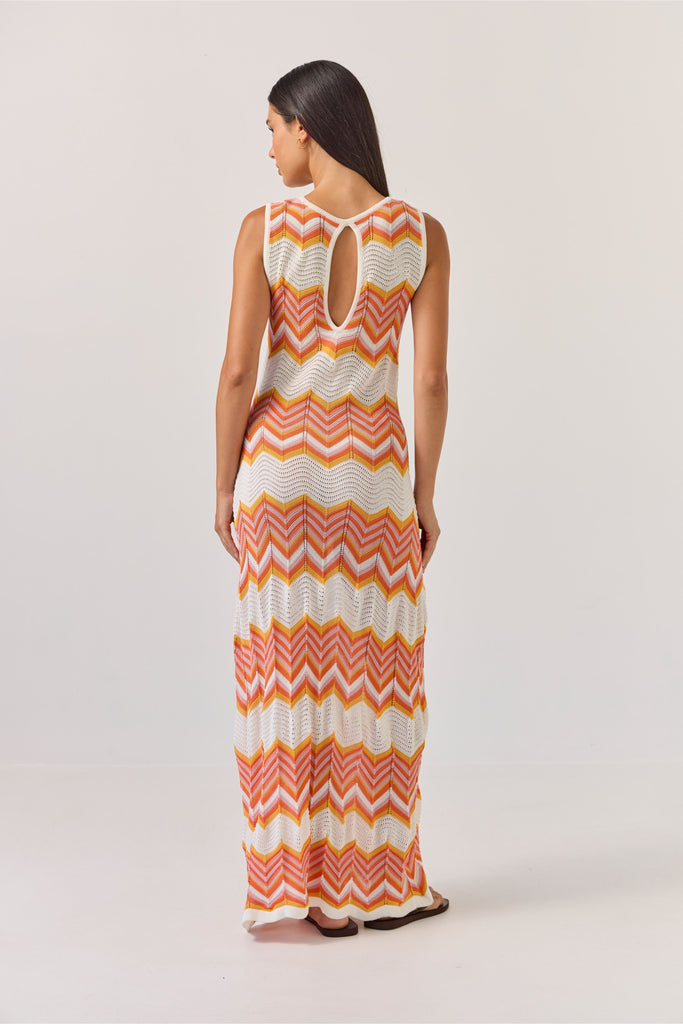 Woman wearing a sleeveless dress with orange and white zigzag pattern on a plain background. Tuesday Label Horizon Dress in a chevron pattern.