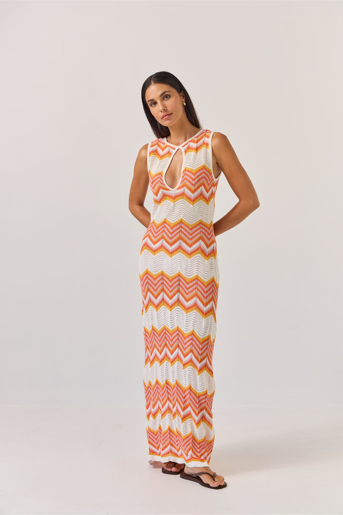 Woman wearing a sleeveless dress with orange and white zigzag pattern on a plain background. Tuesday Label Horizon Dress in a chevron pattern.