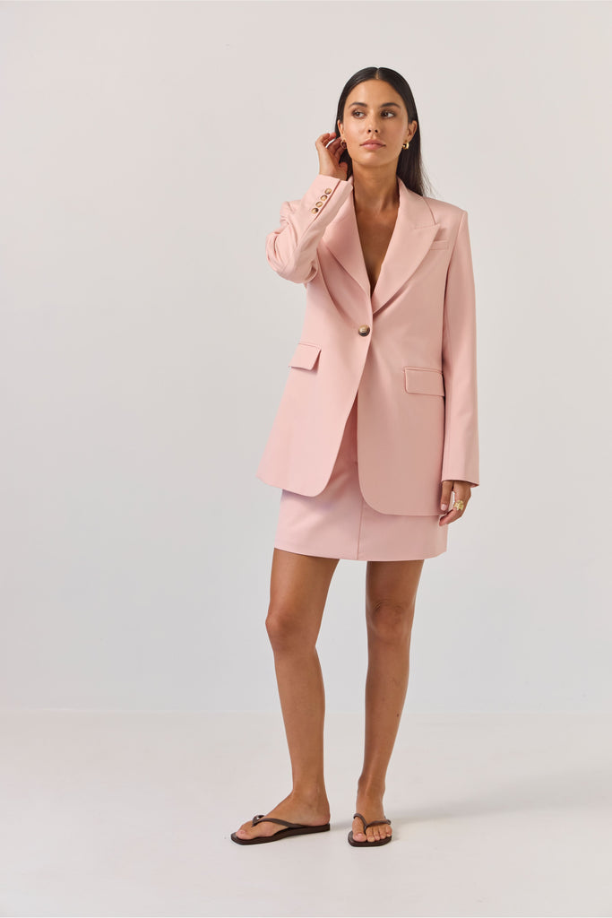 Woman wearing a light pink blazer against a plain background. Tuesday Label Paris Blazer Petal Pink.