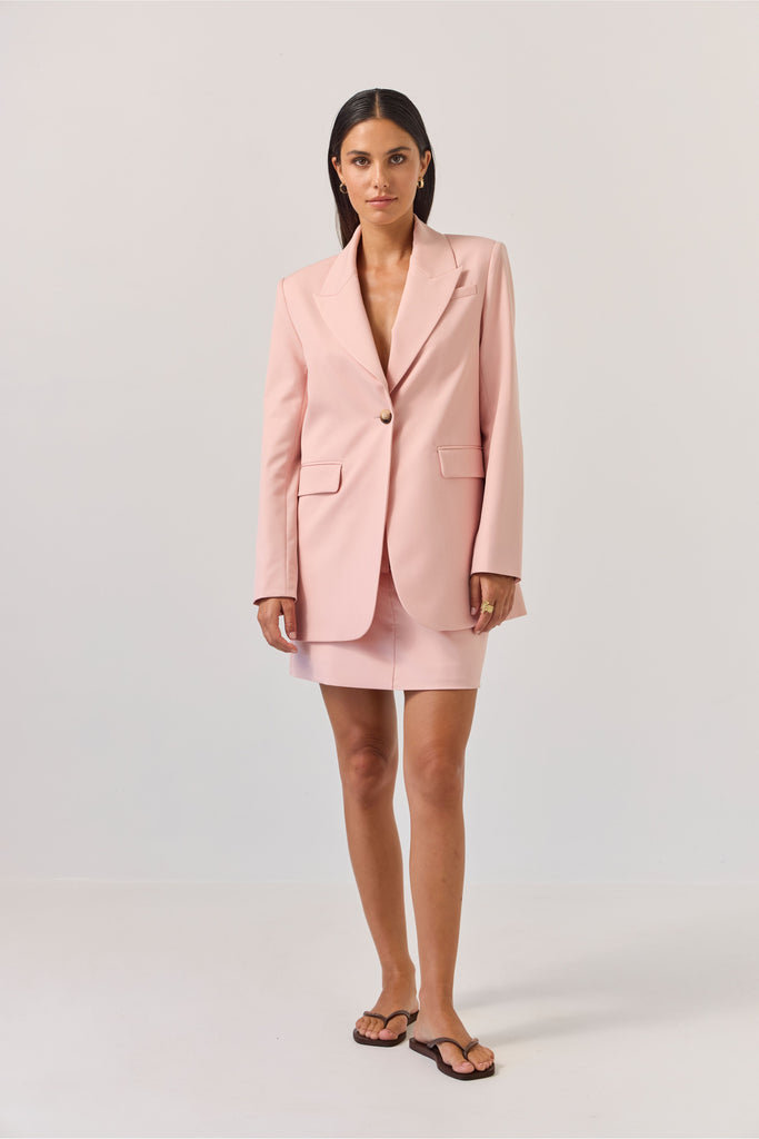 Woman wearing a light pink blazer against a plain background. Tuesday Label Paris Blazer Petal Pink.