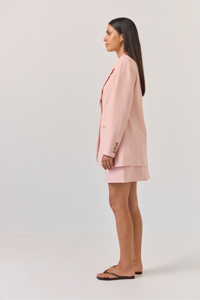 Woman wearing a light pink blazer against a plain background. Tuesday Label Paris Blazer Petal Pink.