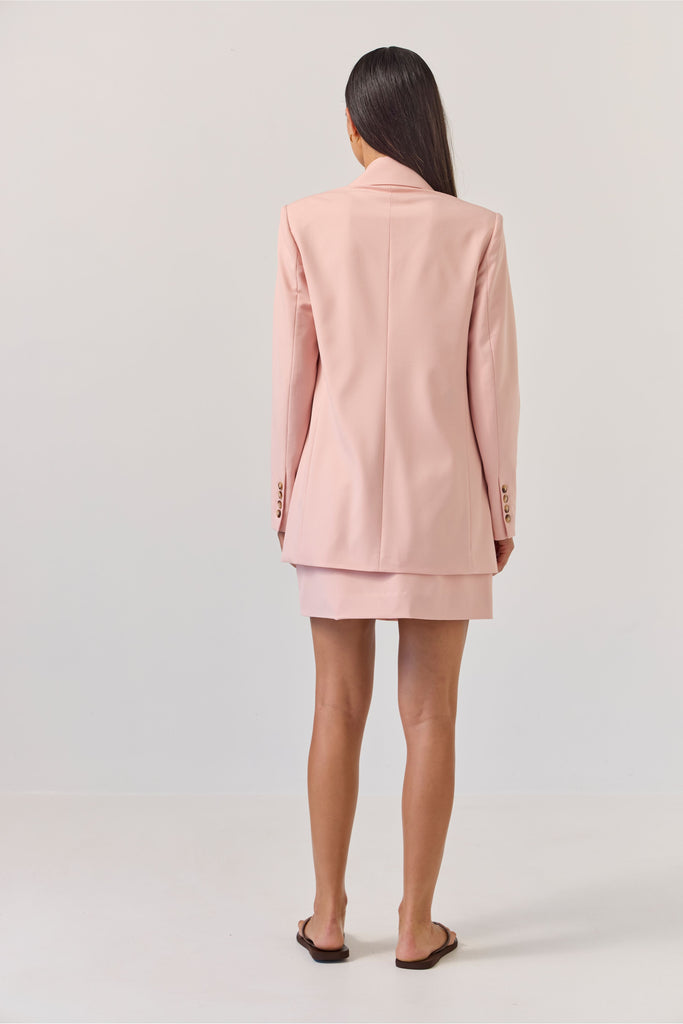Woman wearing a light pink blazer against a plain background. Tuesday Label Paris Blazer Petal Pink.