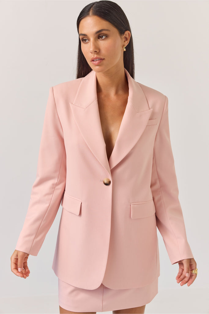 Woman wearing a light pink blazer against a plain background. Tuesday Label Paris Blazer Petal Pink.