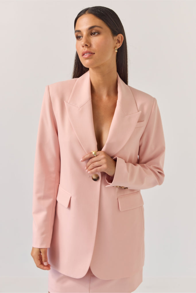 Woman wearing a light pink blazer against a plain background. Tuesday Label Paris Blazer Petal Pink.