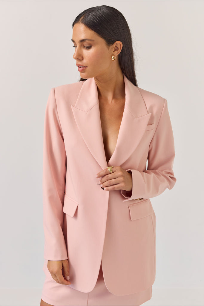 Woman wearing a light pink blazer against a plain background. Tuesday Label Paris Blazer Petal Pink.