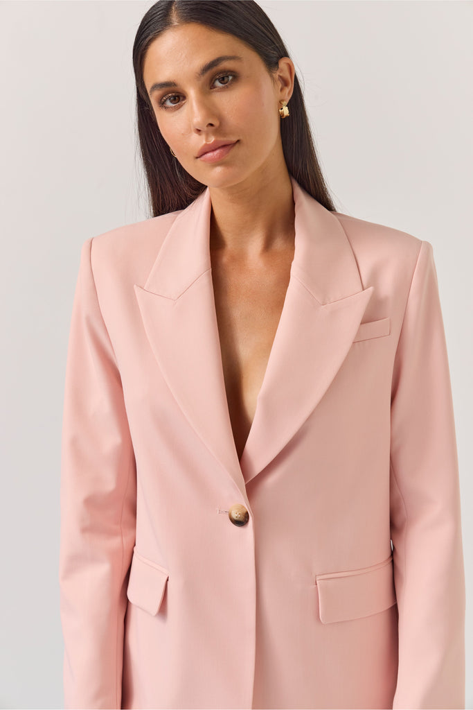 Woman wearing a light pink blazer against a plain background. Tuesday Label Paris Blazer Petal Pink.