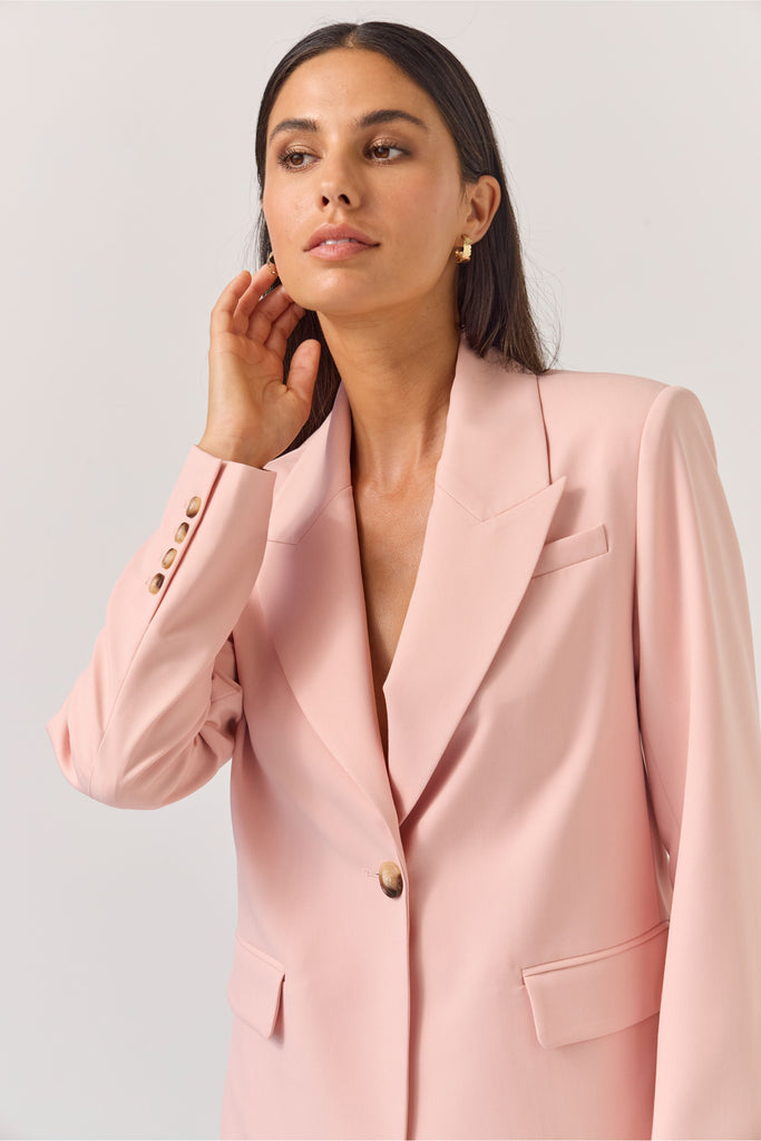 Woman wearing a light pink blazer against a plain background. Tuesday Label Paris Blazer Petal Pink.