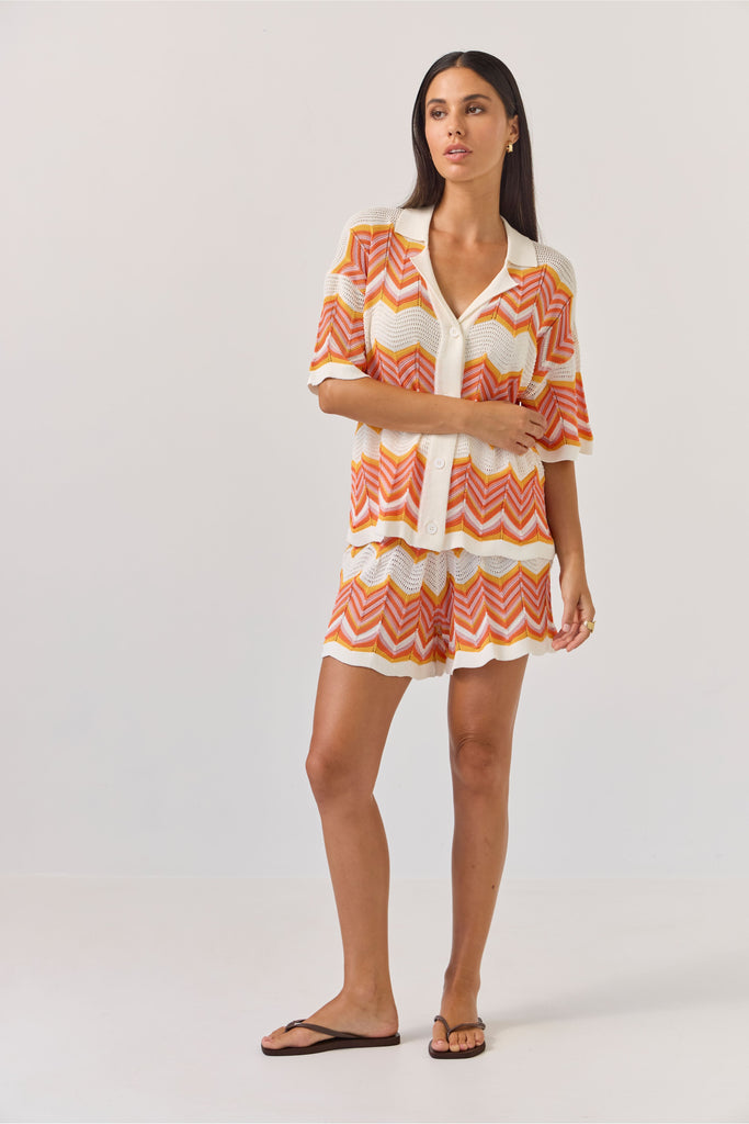 Woman wearing a colourful zigzag patterned matching shirt and shirts on a white background. Tuesday Label Revere Top and Umpire Shorts in chevron pattern.